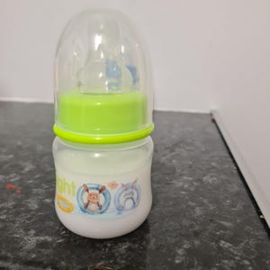 Peut inclure: Un biberon transparent avec un couvercle vert et une t&eacute;tine en silicone. Le biberon a un motif de dessin anim&eacute; d'un lapin et d'un ours portant des bou&eacute;es.