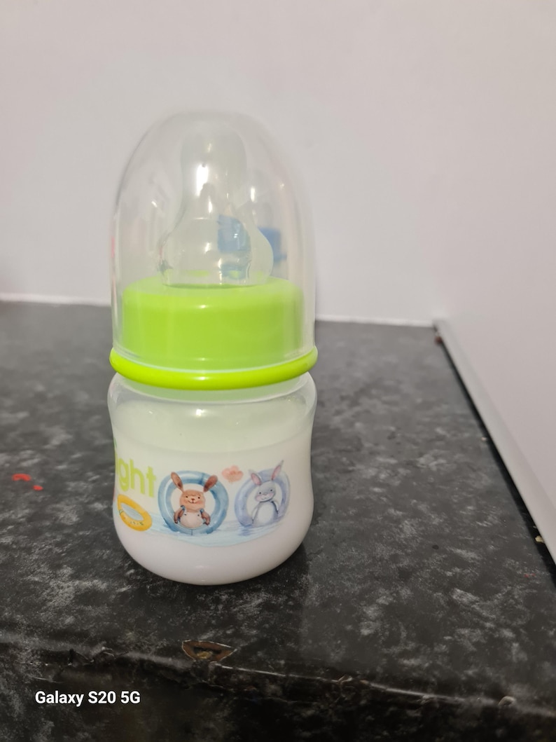 Peut inclure: Un biberon transparent avec un couvercle vert et une t&eacute;tine en silicone. Le biberon a un motif de dessin anim&eacute; d'un lapin et d'un ours portant des bou&eacute;es.