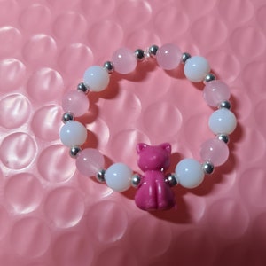 K&ouml;nnte beinhalten: Ein rosa-wei&szlig;es Perlenarmband mit einem rosa Katzenanh&auml;nger. Das Armband besteht aus kleinen runden Perlen und silbernen Zwischenst&uuml;cken.