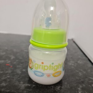 Peut inclure: Un biberon transparent avec un couvercle vert et une &eacute;tiquette blanche sur laquelle est inscrit "griptight". Le biberon est d&eacute;cor&eacute; d'un motif color&eacute; avec un personnage de dessin anim&eacute; et un anneau.