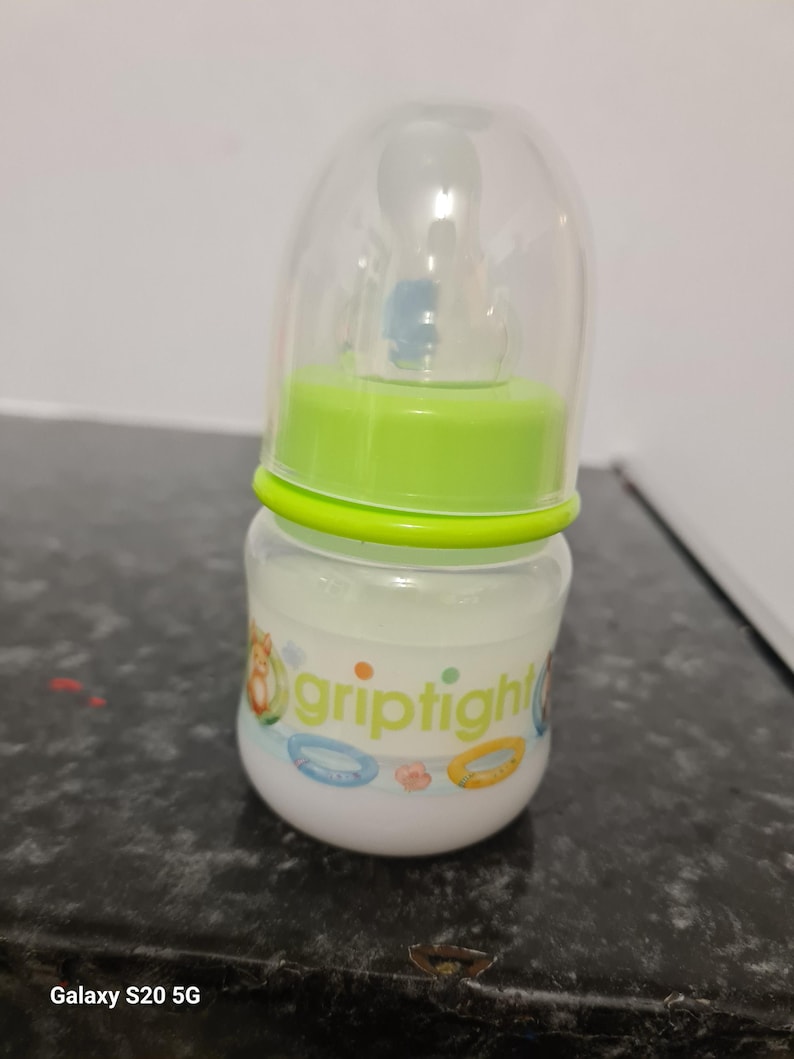 Peut inclure: Un biberon transparent avec un couvercle vert et une &eacute;tiquette blanche sur laquelle est inscrit "griptight". Le biberon est d&eacute;cor&eacute; d'un motif color&eacute; avec un personnage de dessin anim&eacute; et un anneau.