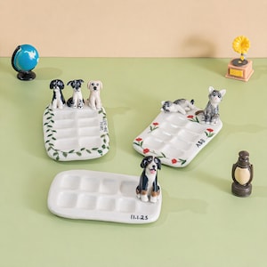 May include: A selection of ceramic trays, each adorned with dog and cat figurines. The white trays feature multiple compartments and decorative details such as leaves and flowers. One tray has the text "Lucas 2016-2023" and another has "11.1.25".