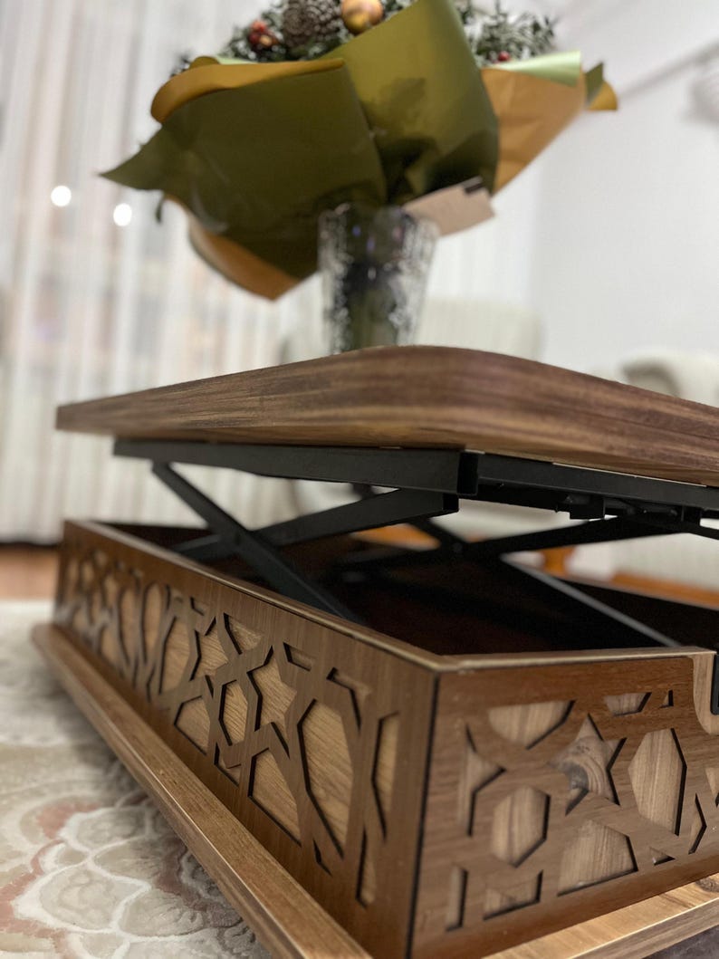 May include: A wooden coffee table with a lift-top mechanism. The table has a geometric pattern carved into the bottom shelf. The table is made of dark wood with black metal accents.