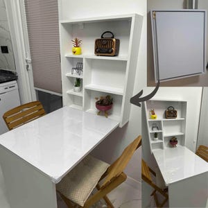 May include: White folding wall-mounted table with shelves. The table is down and has two chairs. The table is white with a glossy finish. The shelves are white and have a variety of items on them, including a radio, plants, and a small shelf.