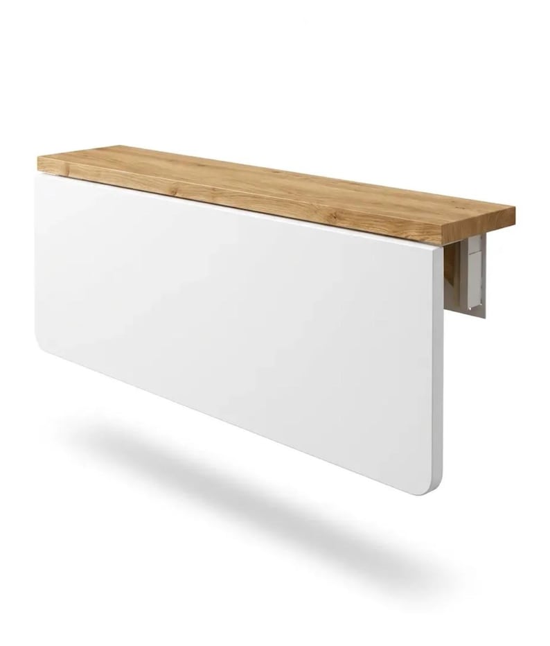 May include: A white, wall-mounted, folding table with a light brown wooden top. The table is rectangular with rounded corners and a simple, modern design. The table is designed to be space-saving.