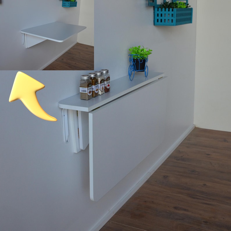 May include: A white, wall-mounted folding table. The table is rectangular and appears to be made of wood. The table is shown in both the folded and unfolded positions. The table is mounted on a white wall. The table is approximately 30 inches long.
