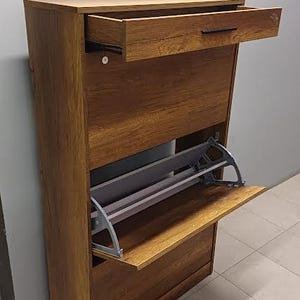 Op de afbeelding: Een bruine houten schoenenkast met een uittrekbare lade en twee planken. De kast heeft een uittrekbaar schoenenrek van grijs metaal.