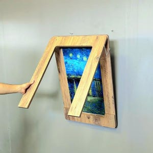 K&ouml;nnte beinhalten: Ein klappbarer Holztisch mit einem Gem&auml;lde der Sternennacht im Rahmen. Der Tisch ist zusammengeklappt und an einer Wand montiert.