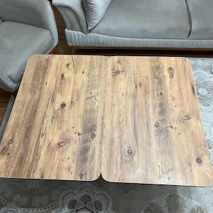 May include: A wooden coffee table with a light brown finish. The table is made of two separate pieces that can be joined together. The table is sitting on a patterned rug.