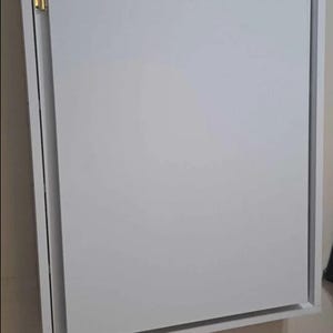 May include: White wall-mounted cabinet with a single door that folds down. The cabinet has a simple design and is made of wood.