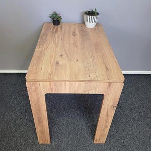 K&ouml;nnte beinhalten: Ein heller Holztisch mit rechteckiger Tischplatte und einem schlichten, modernen Design. Der Tisch hat eine helle Holzoptik und wird von vier Beinen getragen.
