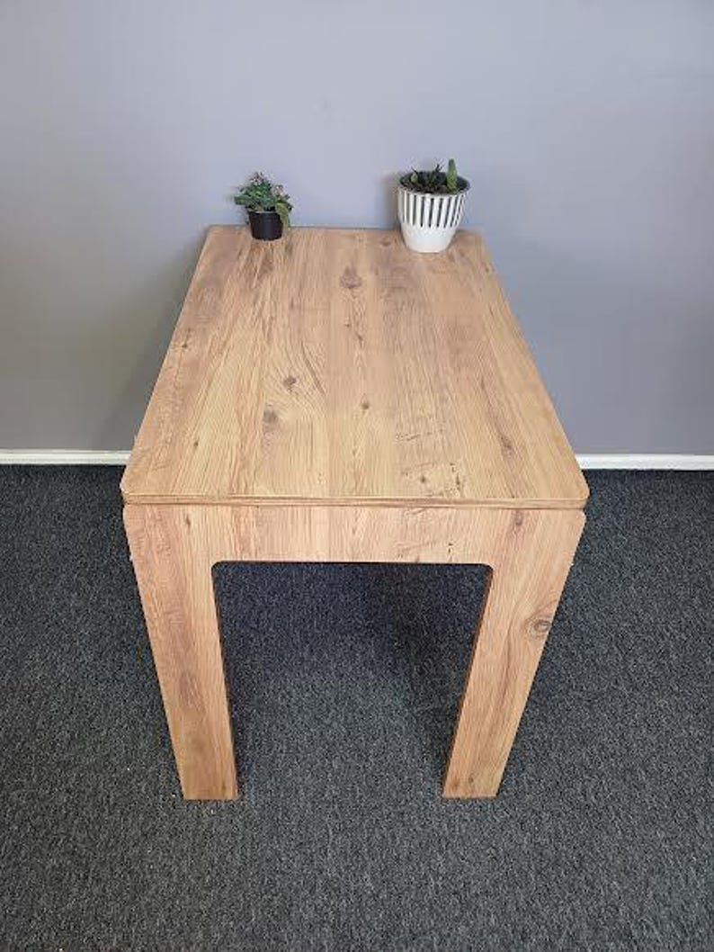 K&ouml;nnte beinhalten: Ein heller Holztisch mit rechteckiger Tischplatte und einem schlichten, modernen Design. Der Tisch hat eine helle Holzoptik und wird von vier Beinen getragen.