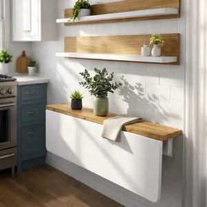 May include: A white and wood-toned wall-mounted drop-leaf table with a wooden top, and two wooden shelves with white ledges. The shelves and table are adorned with plants and vases, creating a modern kitchen aesthetic.