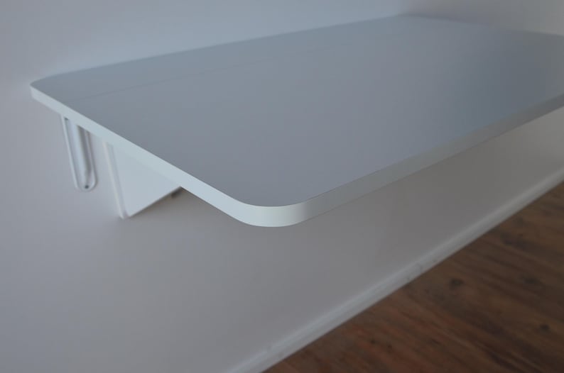 May include: A white floating shelf mounted on a white wall. The shelf has a rounded edge and is supported by a white bracket. The shelf is approximately 24 inches wide and 12 inches deep.