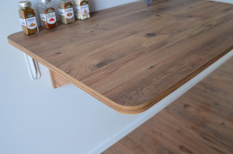 May include: A wooden countertop with a light brown wood grain finish. The countertop is attached to a white surface with metal supports. Several spice jars are on the countertop.