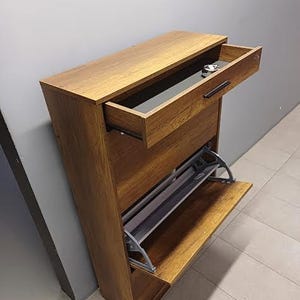 Op de afbeelding: Een bruine houten schoenenrek met een lade en twee planken. De lade is open en de planken zijn leeg.