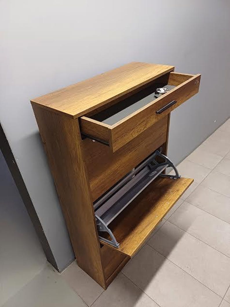 Op de afbeelding: Een bruine houten schoenenrek met een lade en twee planken. De lade is open en de planken zijn leeg.