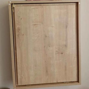 May include: A light wood wall-mounted cabinet with a single door that is closed. The cabinet has a simple design with a light wood finish.