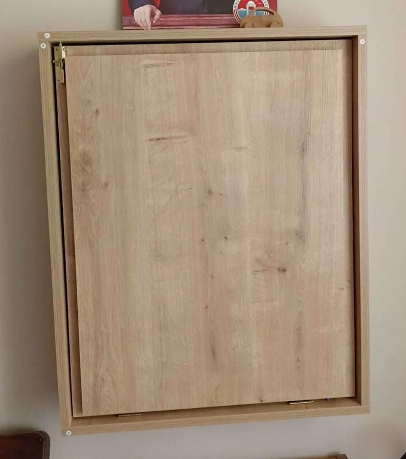 May include: A light wood wall-mounted cabinet with a single door that is closed. The cabinet has a simple design with a light wood finish.