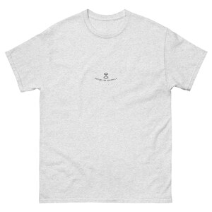 Könnte beinhalten: Hellgraues T-Shirt mit einer kleinen Hammergrafik und dem Text "VICTORY DE VALHALLA" in einem geschwungenen Design. Das Shirt besteht aus einem weichen Material und hat einen klassischen Rundhalsausschnitt.