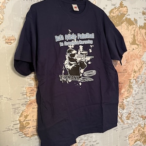 May include: Navy blue t-shirt with the text "Ich spiele Paintball in Sternebeck Harnekup" and a graphic of a paintball player. The shirt also features the text "TIPMANN WSS."