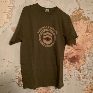 May include: A green t-shirt with a circular logo that says "Tippmann Sports Performance. First in Scenario. Rest in Prior." The logo features a red star and a military-style insignia.