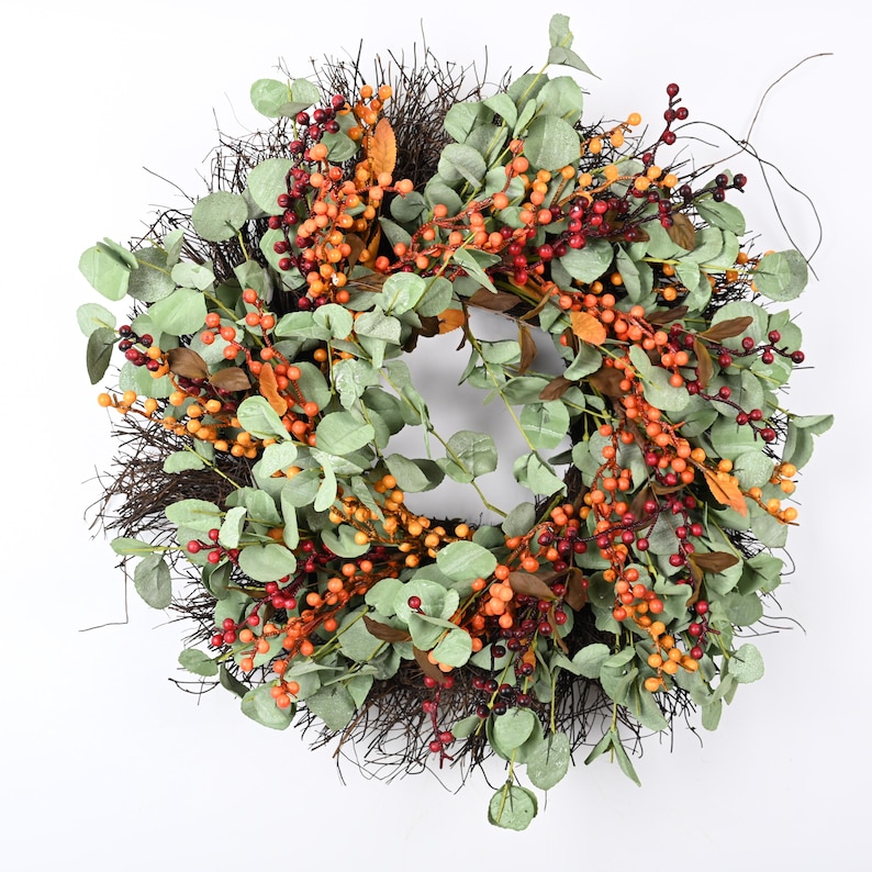 May include: A brown twig wreath decorated with green eucalyptus leaves and red, orange, and yellow berries.
