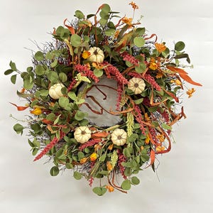 Könnte beinhalten: Ein Herbstkranz mit brauner Basis, verziert mit grünen Eukalyptusblättern, orangefarbenen und roten Blüten und weißen Kürbissen.