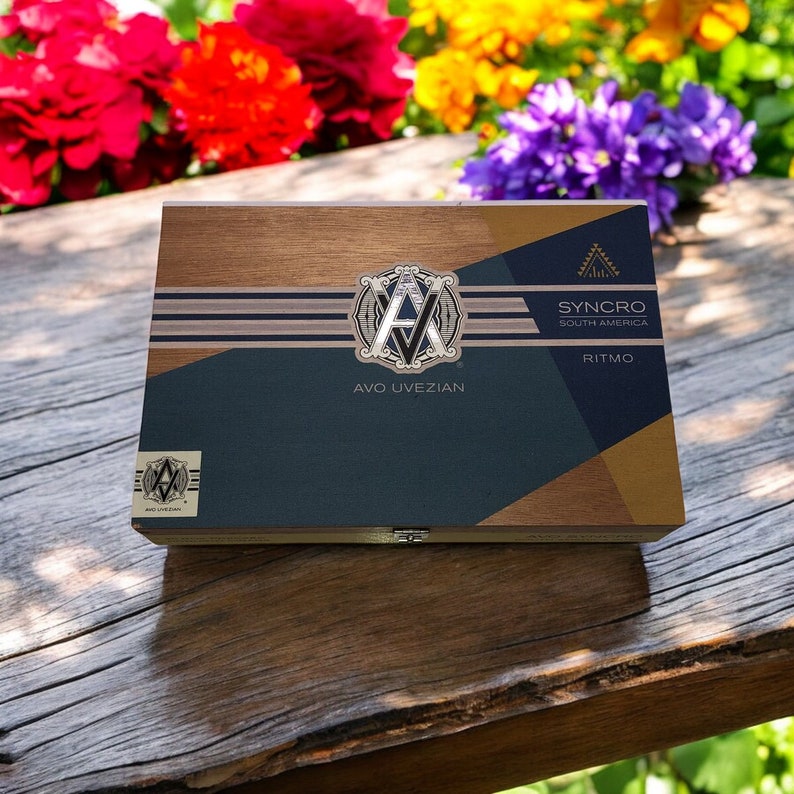 Puede incluir: Una caja de madera con un dise&ntilde;o dorado, azul y blanco. La caja tiene el texto "AVO UVEZIAN" y "SYNCHRO SOUTH AMERICA RITMO" en ella.