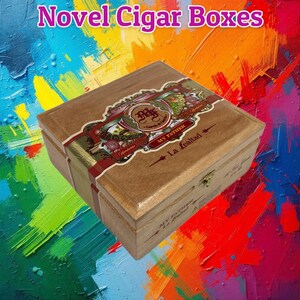 May include: A wooden cigar box with a hinged lid, featuring the text Novel Cigar Boxes at the top. The box displays a decorative label with the words My Father and La Lealtad, along with intricate illustrations and gold-toned metal hardware.
