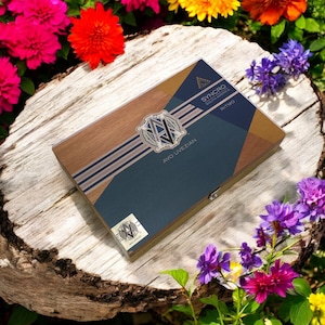 Puede incluir: Una caja de madera con un dise&ntilde;o azul y dorado. La caja tiene el texto "AVO UVEZIAN" y "SYNCHRO SOUTH AMERICA" en ella. La caja est&aacute; sentada sobre una superficie de madera con flores alrededor.