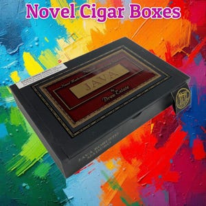 Könnte beinhalten: Eine schwarze, rechteckige Zigarrenkiste mit einem zentralen Etikett, das den Text JAVA by Drew Estate, Hand Made und Premium Long Filler enthält. Die Kiste hat einen Warnhinweis und den Text JAVA ROBUSTO MADURO an der Seite.