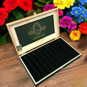 May include: An open wooden box with a green interior and a black velvet lining. The box has a hinged lid with gold lettering and the words "andalusian bull". The box is surrounded by colorful flowers.