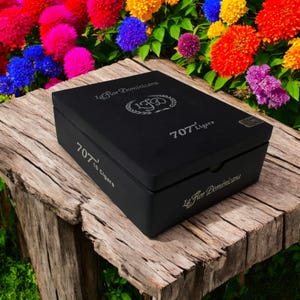 May include: A black wooden box with a silver label that reads "La Flor Dominicana 707 Ligero 10 Cigars". The box is sitting on a wooden surface.