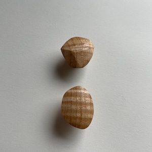 Puede incluir: Dos pomos de madera, uno con forma de diamante redondeado y el otro con forma ovalada. Ambos pomos son de color marrón claro y tienen un patrón de veta de madera.