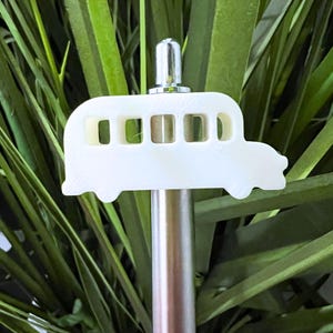May include: White plastic school bus shaped bottle stopper with a silver top. The stopper is attached to a silver metal rod.