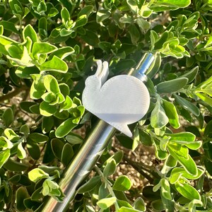 May include: A white plastic snail-shaped pen topper attached to a silver pen.