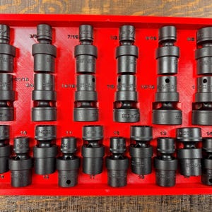 Könnte beinhalten: Eine rote Ablage mit einem Satz schwarzer Schlagschraubernüsse. Die Nüsse sind in Reihen und Spalten angeordnet, mit verschiedenen Größen und Markierungen. Die Ablage besteht aus rotem Material, und die Nüsse sind aus einem dunklen, haltbaren Metall.