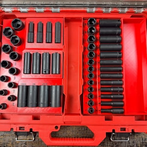 Op de afbeelding: Een rode gereedschapskist met een doorzichtig deksel, gevuld met een verscheidenheid aan zwarte doppen en verlengstukken. De doppen zijn gerangschikt in georganiseerde compartimenten, met verschillende maten. De gereedschapskist is open en onthult de gereedschappen binnenin.