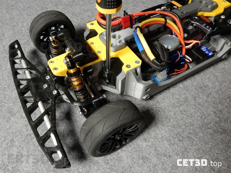 May include: A partially assembled gray and yellow RC car chassis with black tires and suspension components. A screwdriver is being used to tighten a screw on the yellow frame. The front bumper is detached. The text "CET3D.top" is visible.