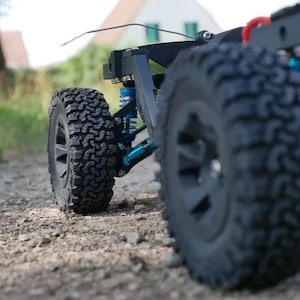 May include: A black and blue off-road vehicle with large tires and a suspension system. The vehicle is on a dirt path.