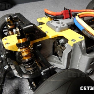 May include: Close-up of a 3D-printed RC car chassis. The chassis features a yellow and gray frame with black suspension components, gold springs, and visible gears. Electrical wiring and the text "CET3D.top" are also visible.