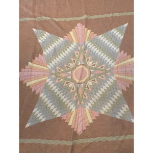 May include: A vintage quilt with a large, multi-colored star design. The star is made up of various shades of pink, peach, green, and gray fabric. The background of the quilt is a solid brown color.