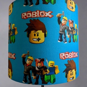 May include: A blue lampshade with a repeating pattern of Roblox characters and the word "Roblox" in red letters.