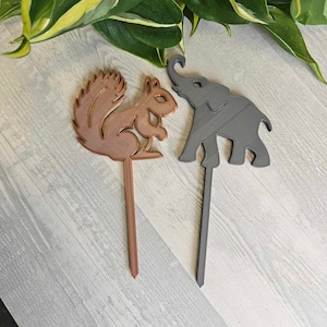 May include: Two wooden animal silhouette cake toppers. A brown squirrel and a gray elephant.