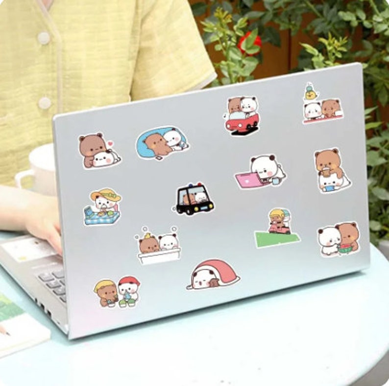 May include: A set of 15 brown and white bear stickers featuring various activities, including driving a car, relaxing in a tent, and taking a bath. The stickers are on a silver laptop.
