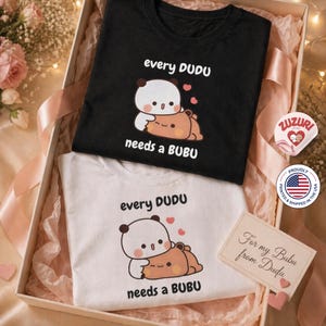 May include: Two t-shirts, one black and one white, inside a gift box. Each shirt features a cartoon panda design with the text "every DUDU needs a BUBU". A small card reads "For my Bubu from Dudu".