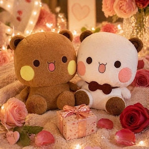 May include: Two plush bear toys, one brown and one white, sit side-by-side. The brown bear has yellow cheeks, and the white bear has pink cheeks and a bow tie. A small gift box with a pink ribbon and roses are in the foreground.