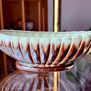 May include: A brown and white ceramic planter with a wavy, ribbed design. The planter is oval shaped and has a glossy finish.