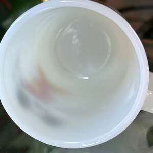 以下が含まれることがあります： 上から見た、白いセラミックマグカップ。マグカップの内側は白く、底にはかすかなデザインが見えます。マグカップはぼやけた背景に置かれています。